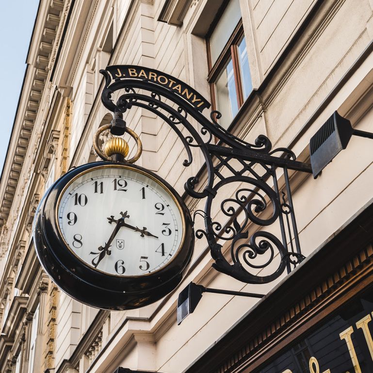 Das Zunftschild an der Fassade von Barot&aacute;nyi symbolisiert die langj&auml;hrige Tradition und Expertise des Uhrmacher- und Juweliergesch&auml;fts.